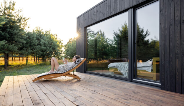 Eine Frau genießt die Abendsonne lesend auf ihrer Holzterrasse